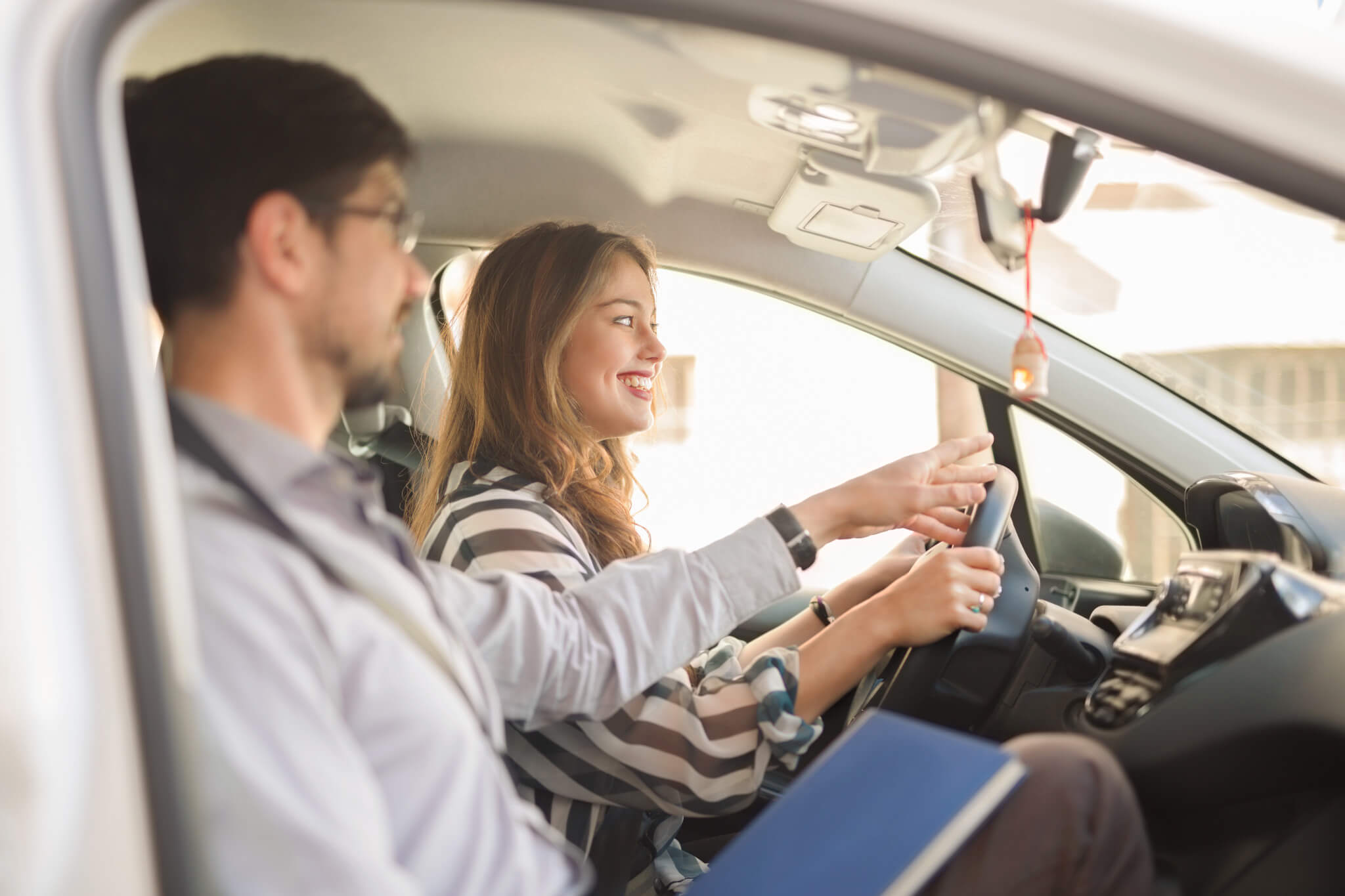 Erste Fahrstunde, Fahrlehrer zeigt Fahrschülerin etwas im Fahrschulauto