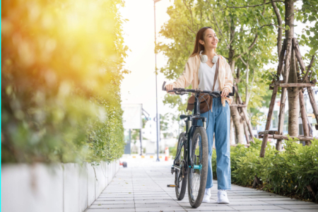 Kopfhörer beim Fahrradfahren, Frau schiebt Fahrrad, lächelt und hat Kopfhörer um ihren Hals