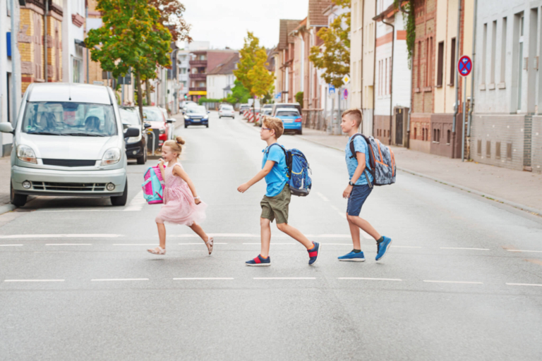 Verkehrserziehung Kinder, Drei Schulkinder laufen über die Straße