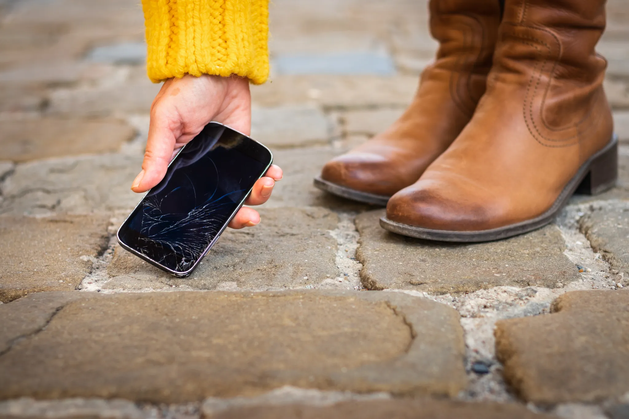 Neuwert, Person hebt Handy mit zerbrochenem Bildschirm auf