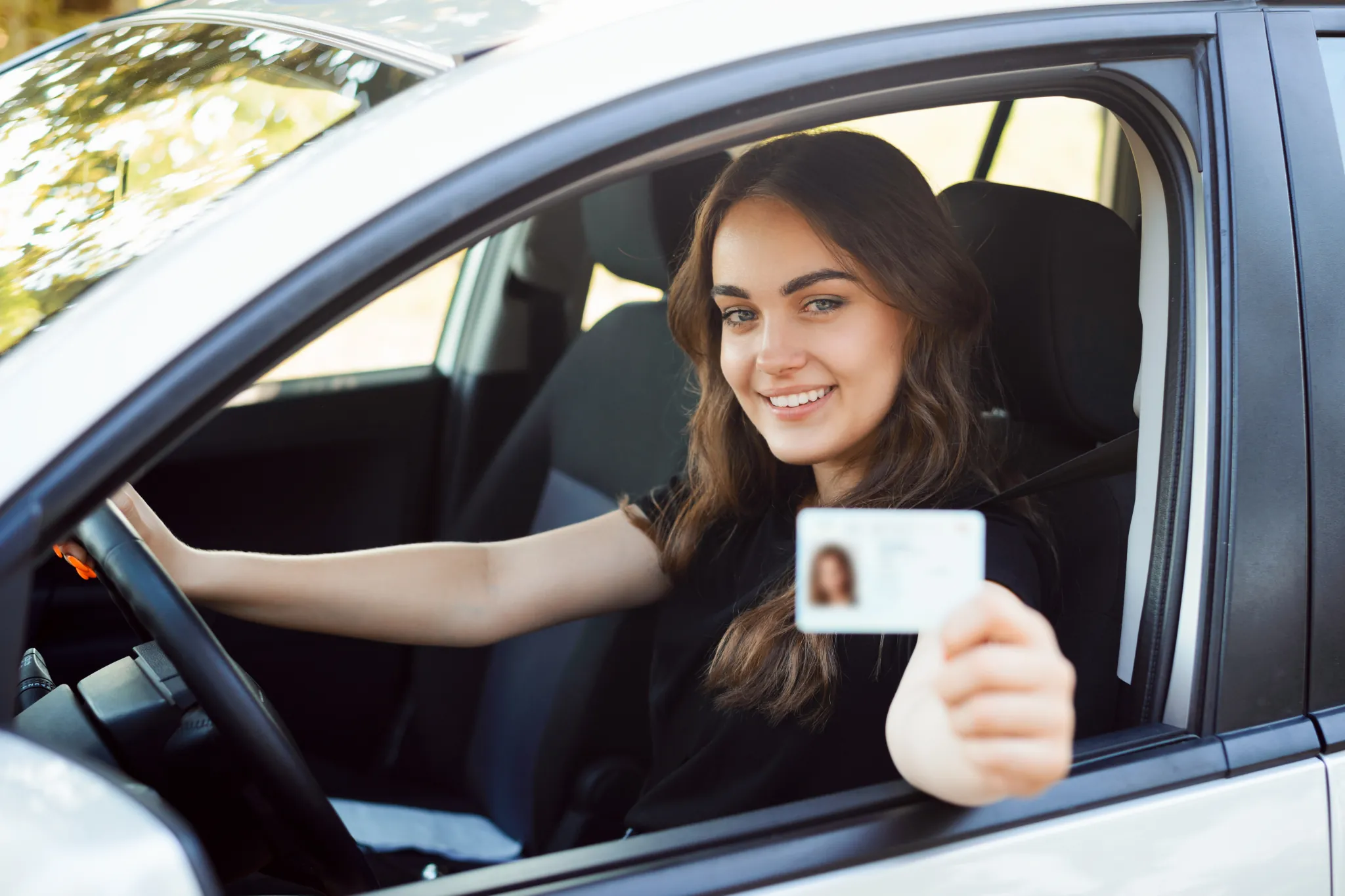 Probezeit Führerschein, Frau hält neuen Führerschein in die Kamera, sitzt hinter dem Steuer eines Autos