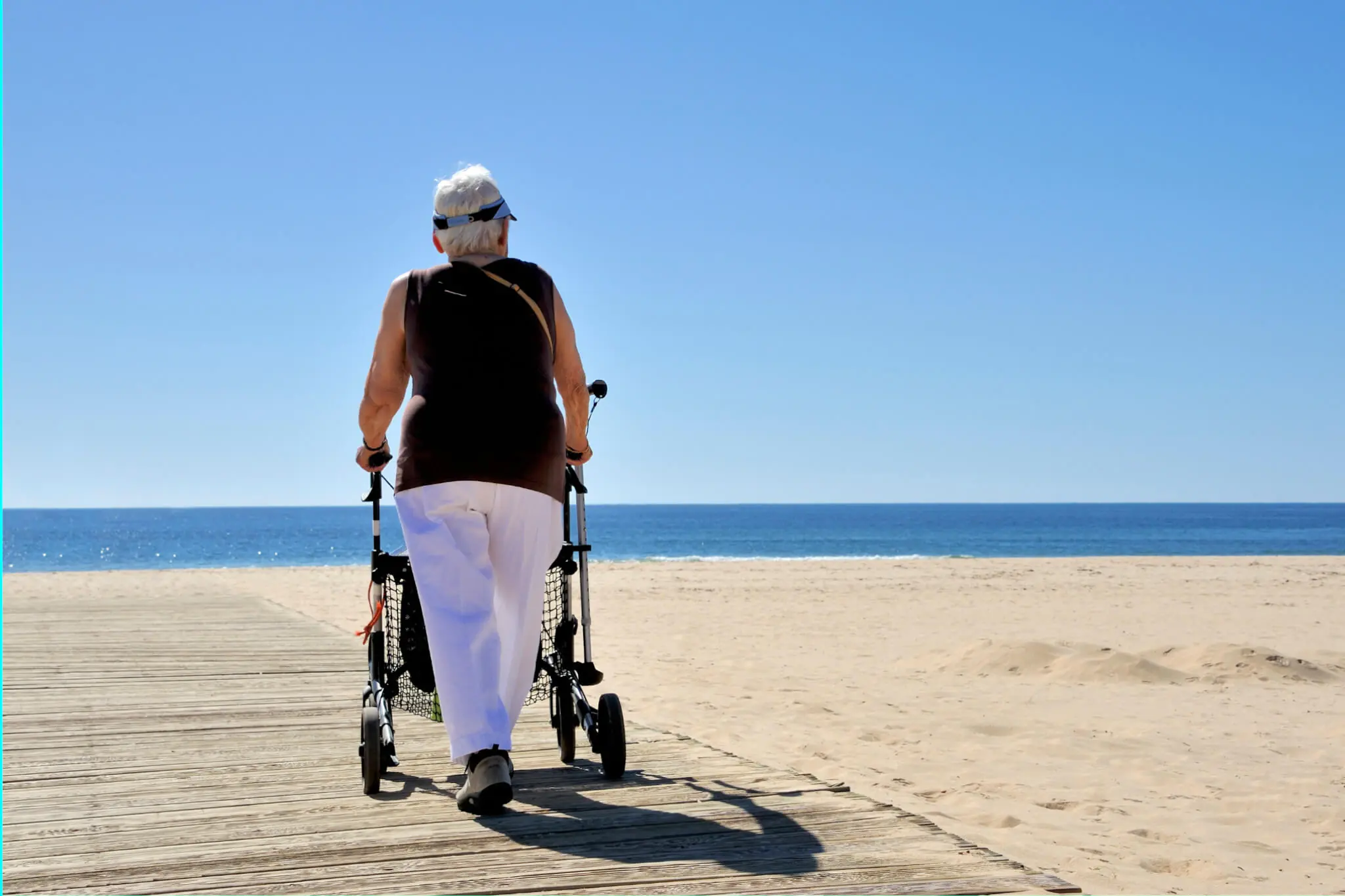 Hilfsmittelversicherung, Ältere Dame geht mit Rollator am Strand spazieren