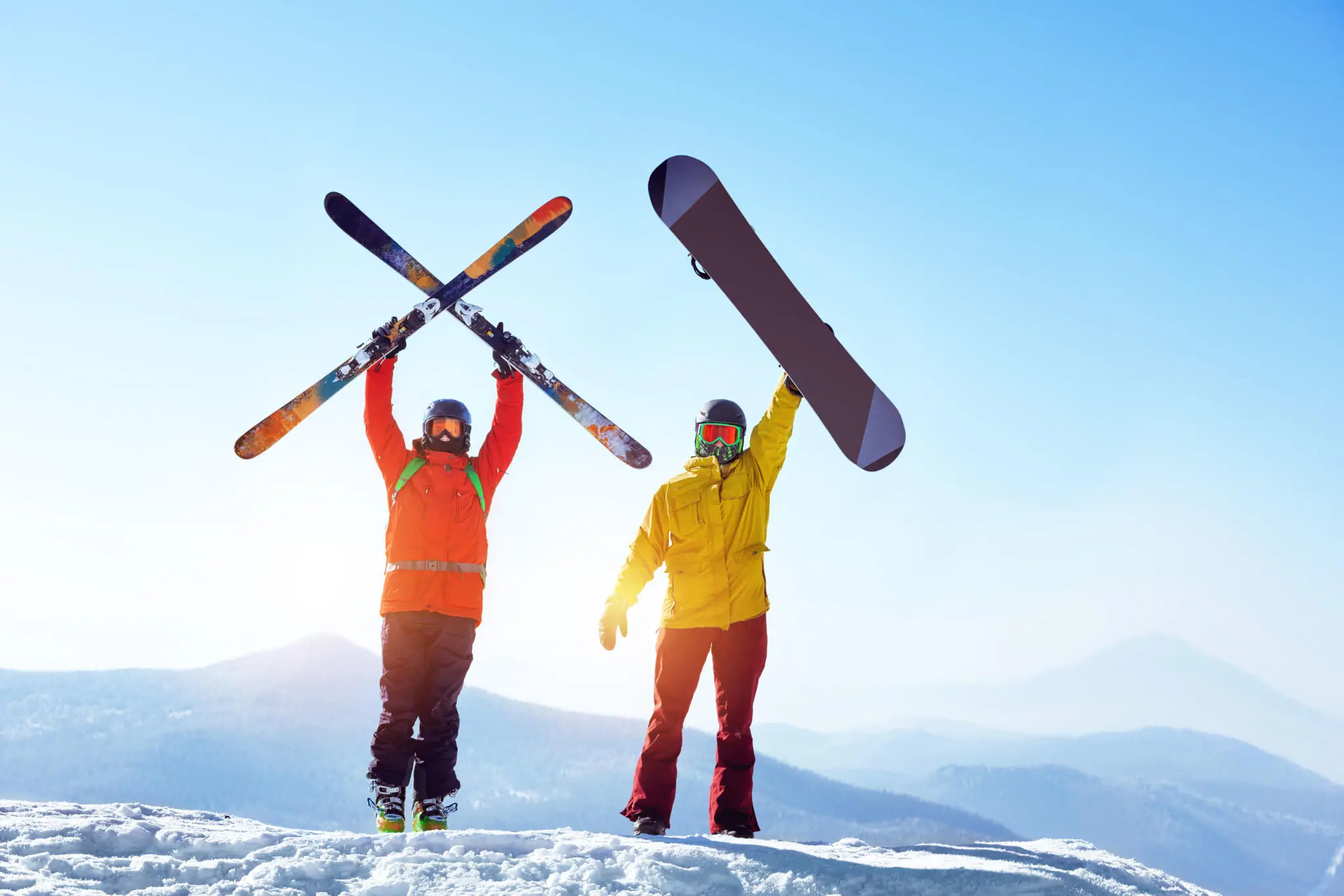 Ski oder Snowboard, 2 Personen auf einem Berg in Wintersportausrüstung, eine hält Skier in die Luft, die andere ein Snowboard