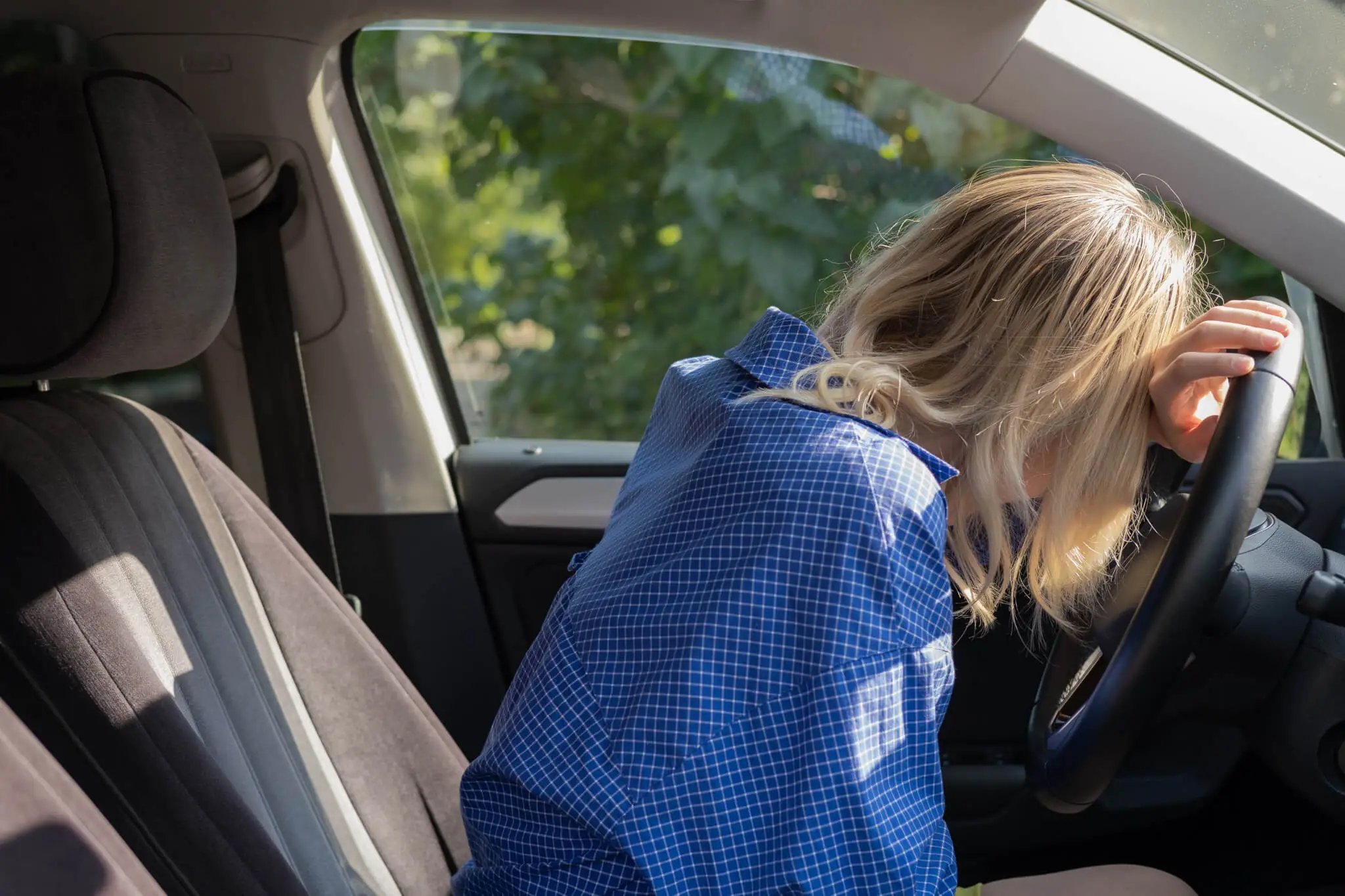 Müdigkeit beim Autofahren, Frau schläft im Auto angelehnt an Lenkrad